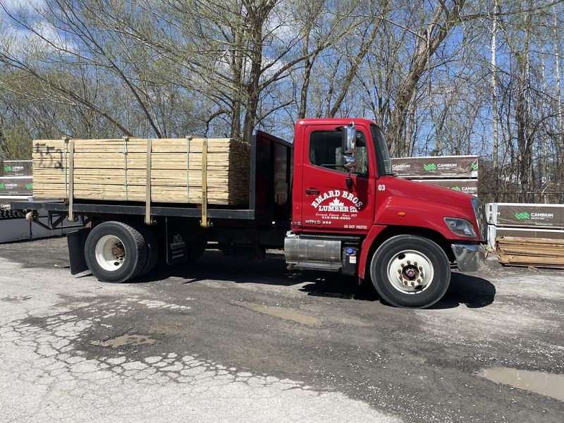 A red Emard Bros. Lumber flatbed truck loaded with framing lumber at the yard