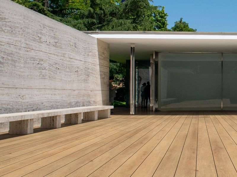 A wide timber deck running toward a modern glass and stone building
