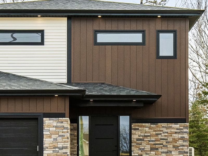 A modern two storey home clad in dark wood siding and stone veneer