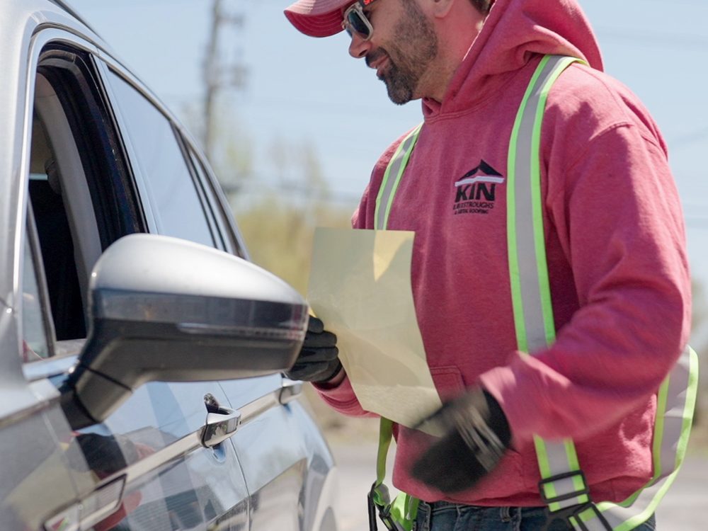 An Emard Bros. Lumber driver in a high visibility jacket checking a delivery slip at a truck window