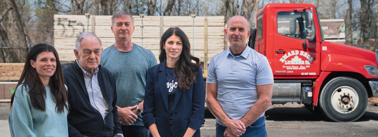 Five members of the Emard family standing in front of stacked lumber and a red delivery truck