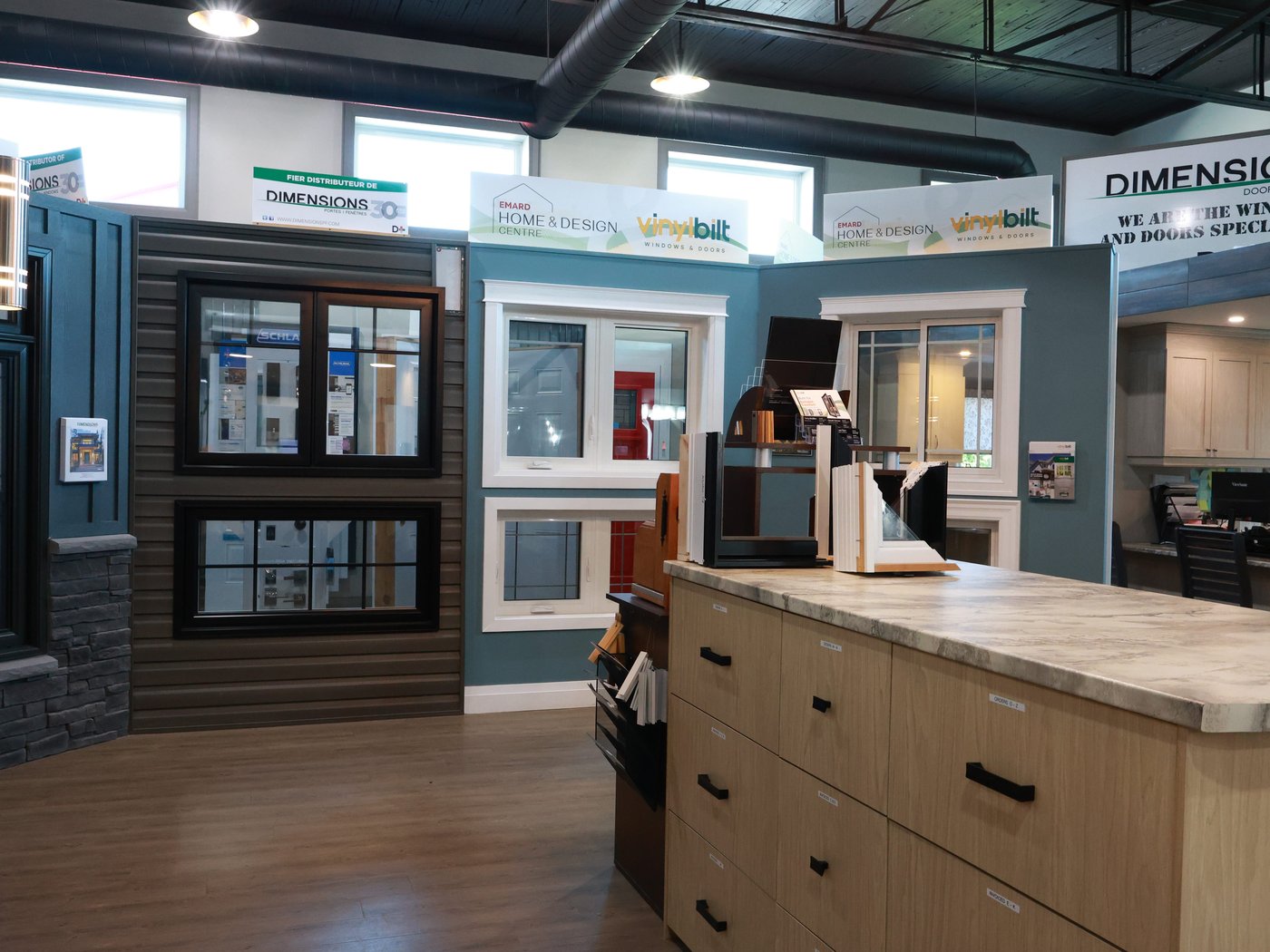 Black and white windows mounted in siding and stone on the Cornwall showroom floor, under the Emard Home & Design Centre sign