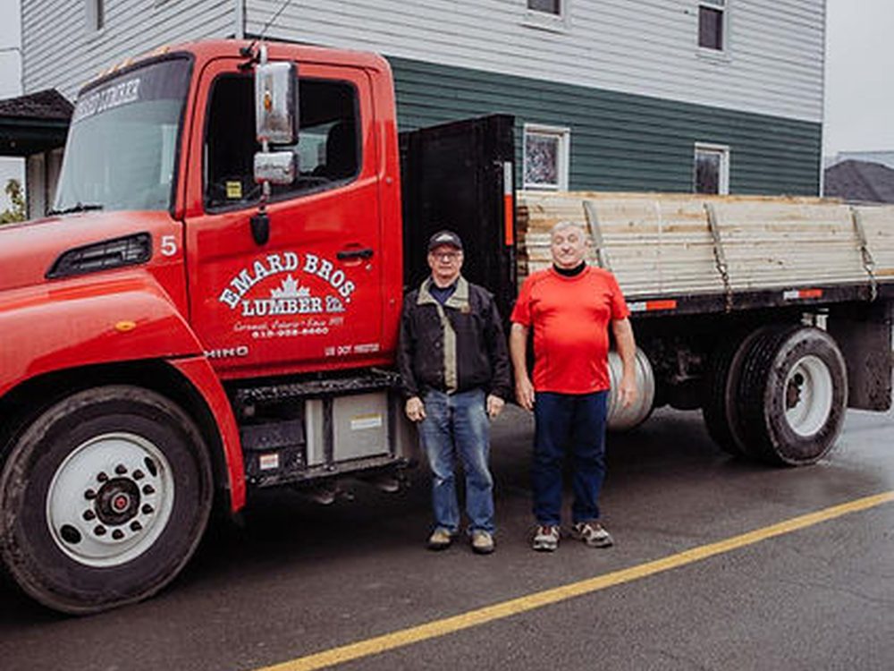 Two Emard Bros. Lumber staff standing beside a red delivery truck loaded with lumber