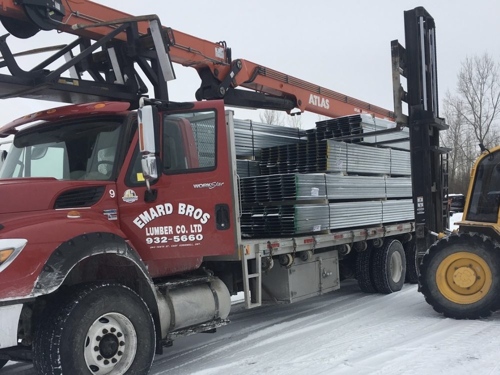 A red Emard Bros. Lumber flatbed truck being loaded by a forklift
